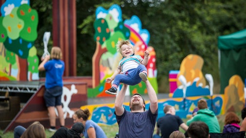 A child laughing while being held in the air by a adult at an open air theatre performance